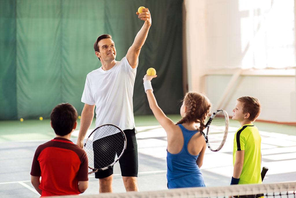 An instructor teaching 1 girl and two boys how to hold the ball for a serve